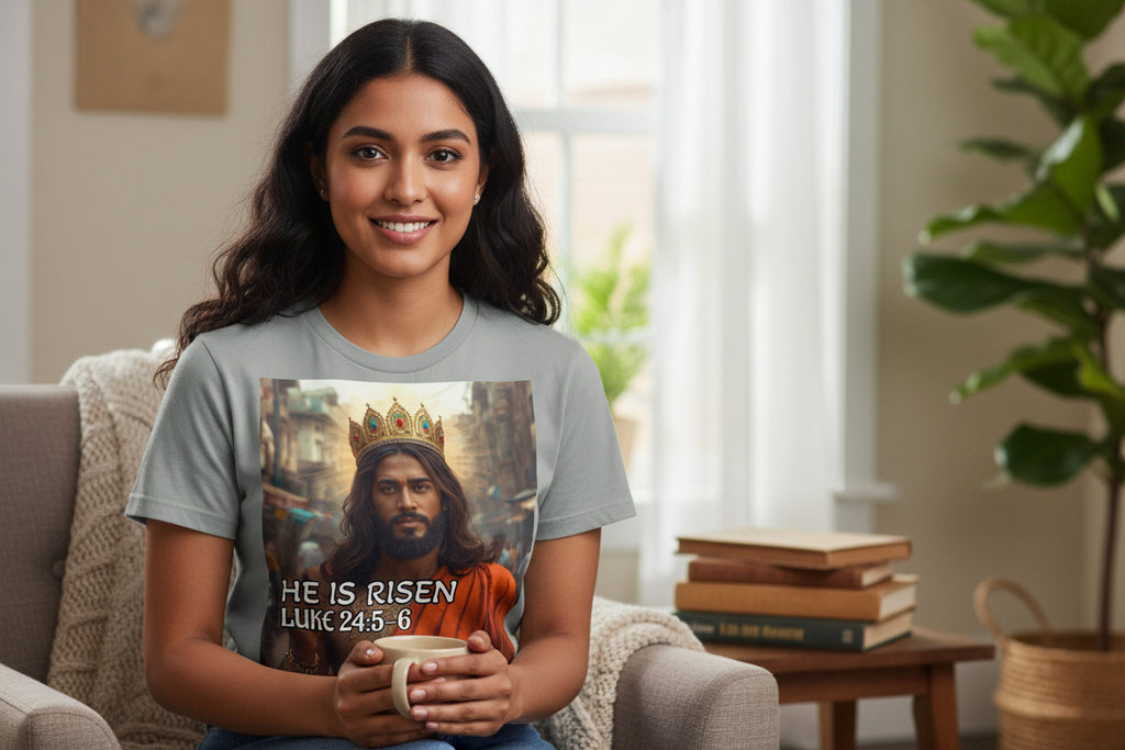 Woman wearing a t-shirt with a Indian Jesus wearing a crown with text 'He Is Risen', holding a mug in a cozy living room.