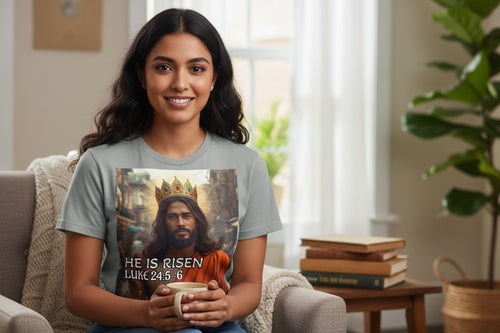 Woman wearing a t-shirt with a Indian Jesus wearing a crown with text 'He Is Risen', holding a mug in a cozy living room.