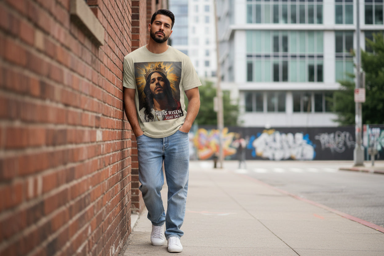 Man wearing a t-shirt with a graphic design of a crowned Hispanic Jesus, standing against a brick wall in an urban setting.