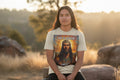 Beige t-shirt with a graphic of a CROWN INDIGENOUS JESUS and 'He is Risen' text on a white background