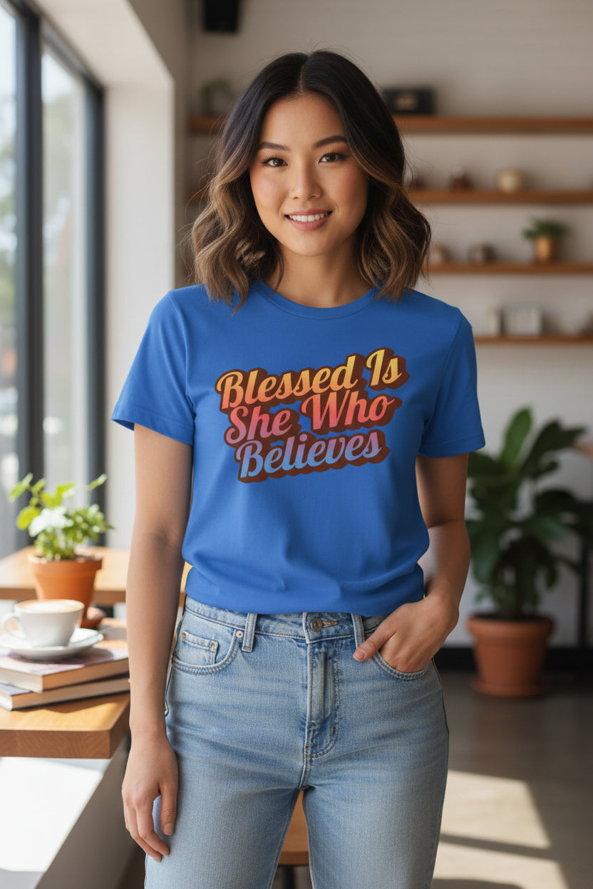 Woman wearing a blue t-shirt with 'Blessed Is She Who Believes' text in a home setting.