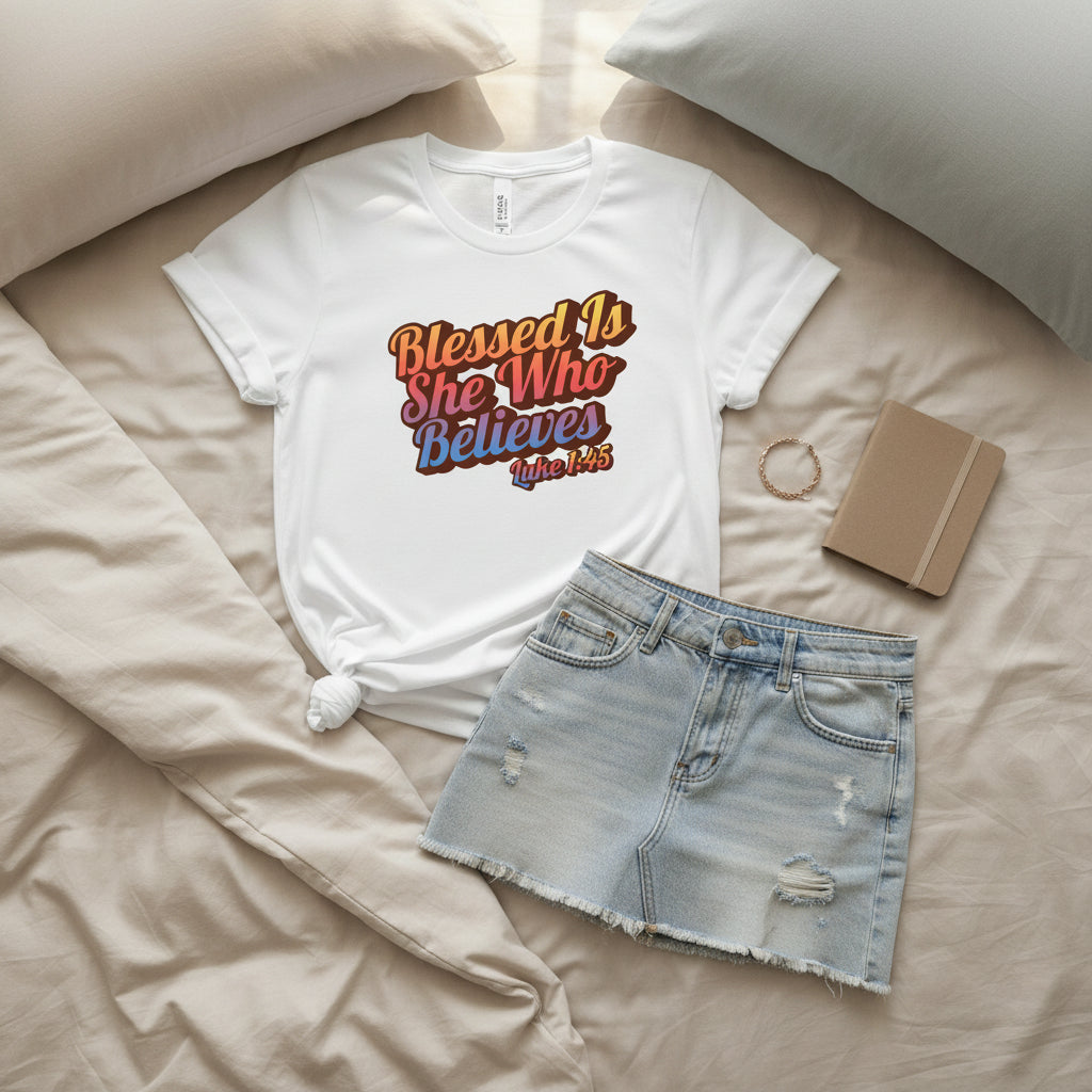 White t-shirt with colorful text 'Blessed Is She Who Believes Luke 1:45' on a white background